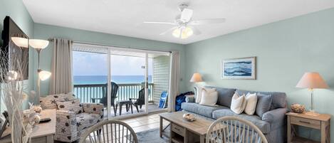 A spacious living room with a view of the ocean, a ceiling fan, and a dining area with a table and chairs.