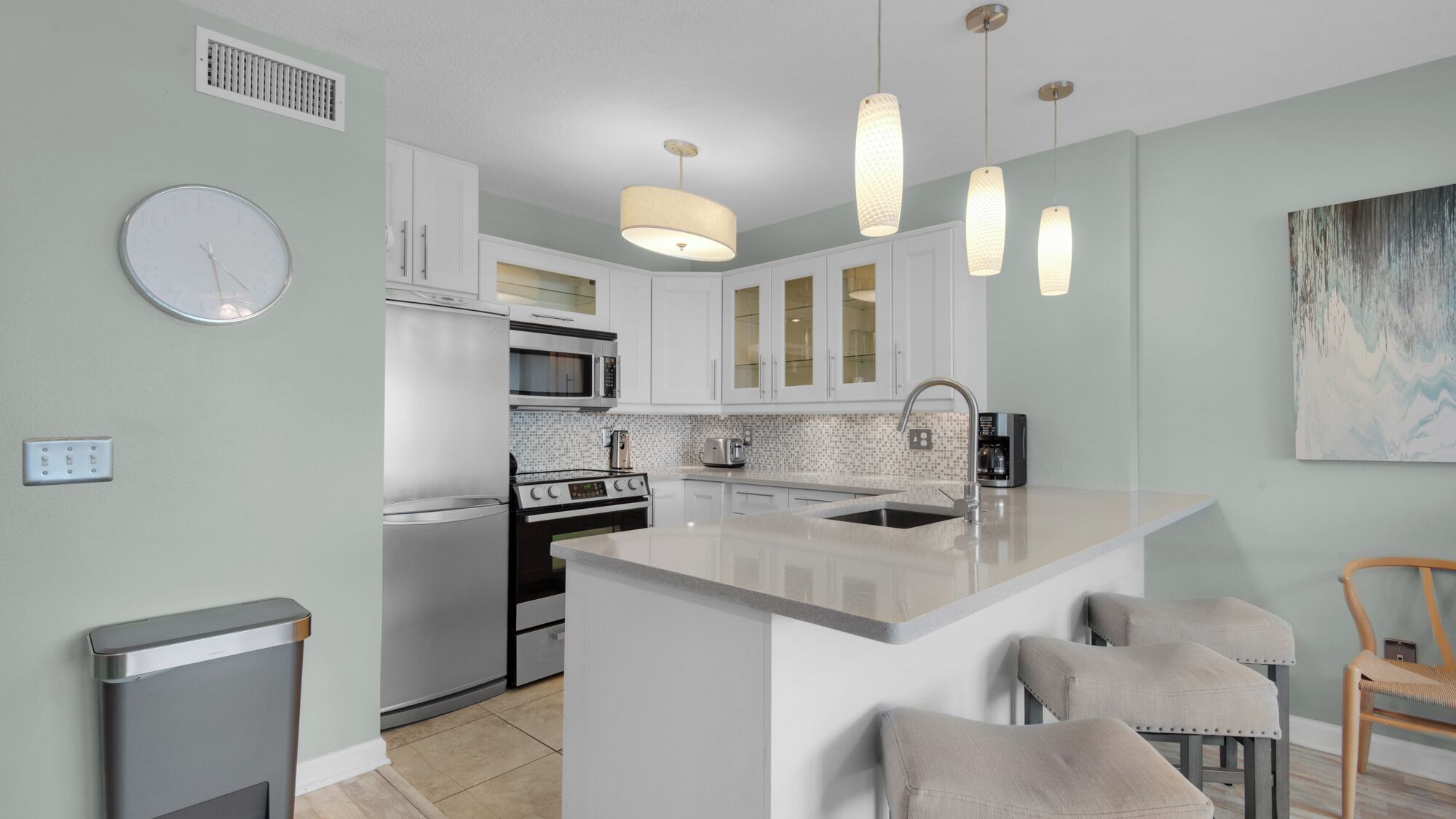 A modern kitchen with white cabinets, a central island with bar stools, a microwave, oven, and a coffee maker.