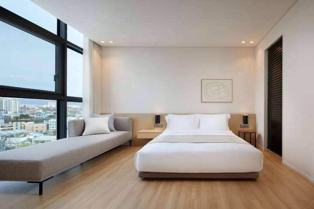Quarto moderno com uma cama grande, um sofá e vista para a cidade.
