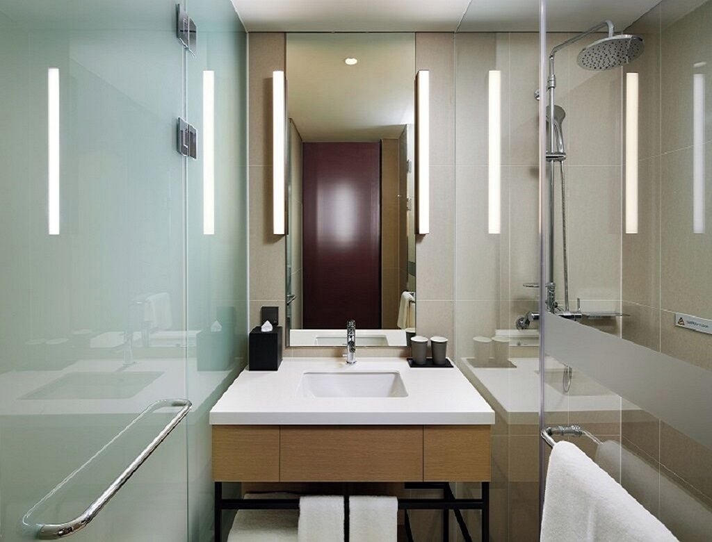 A modern bathroom with a glass shower enclosure, a large mirror, a white sink, and a towel rack.