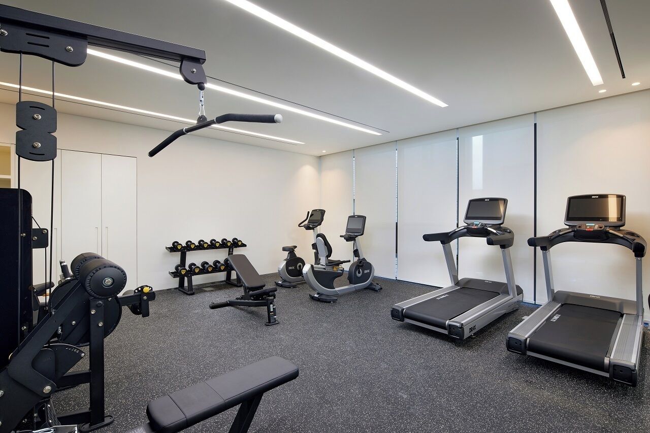 A modern gym with cardio machines, free weights, and a bench.