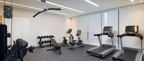 A modern gym with cardio machines, free weights, and a bench.