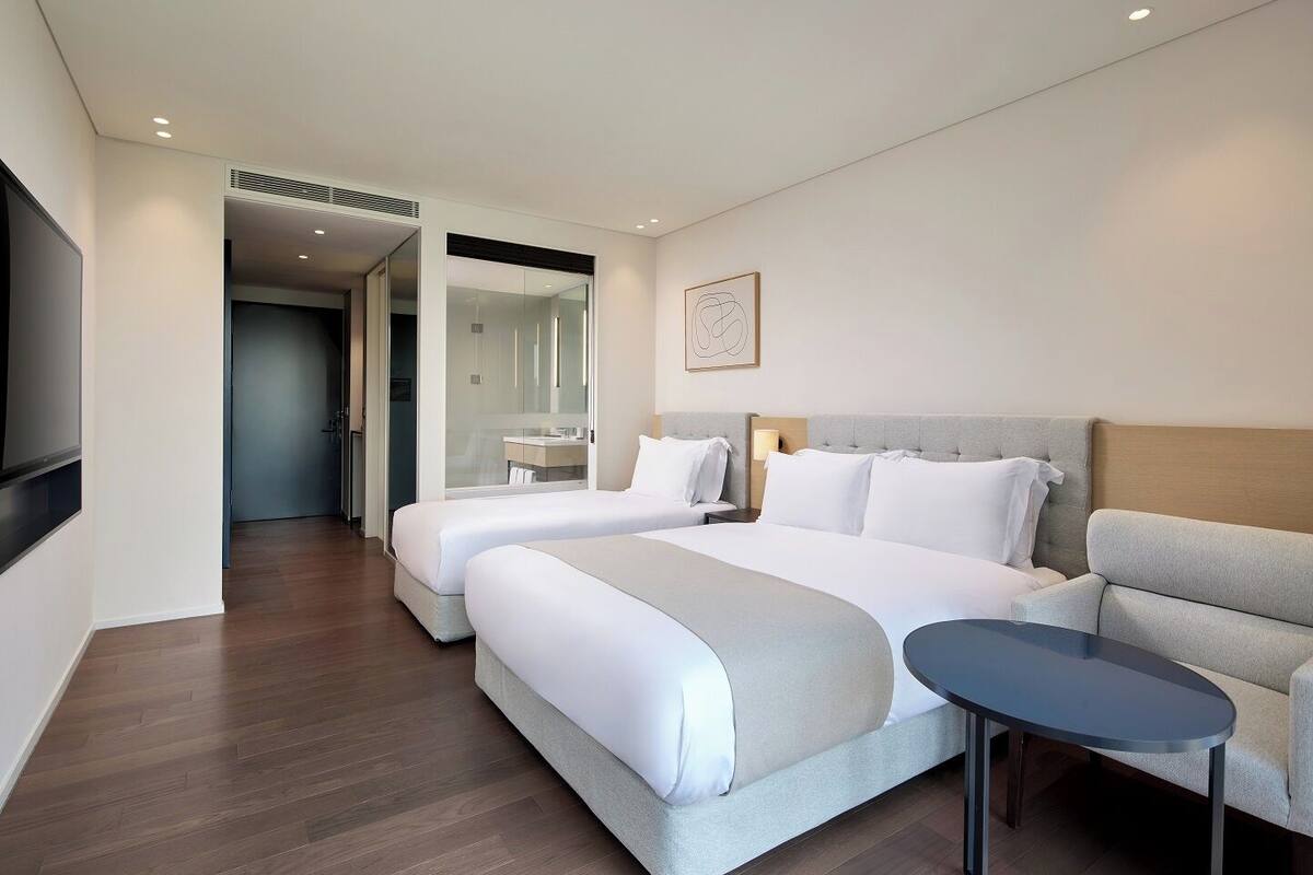 Quarto de hotel com duas camas, um sofá, uma mesa pequena e uma televisão.