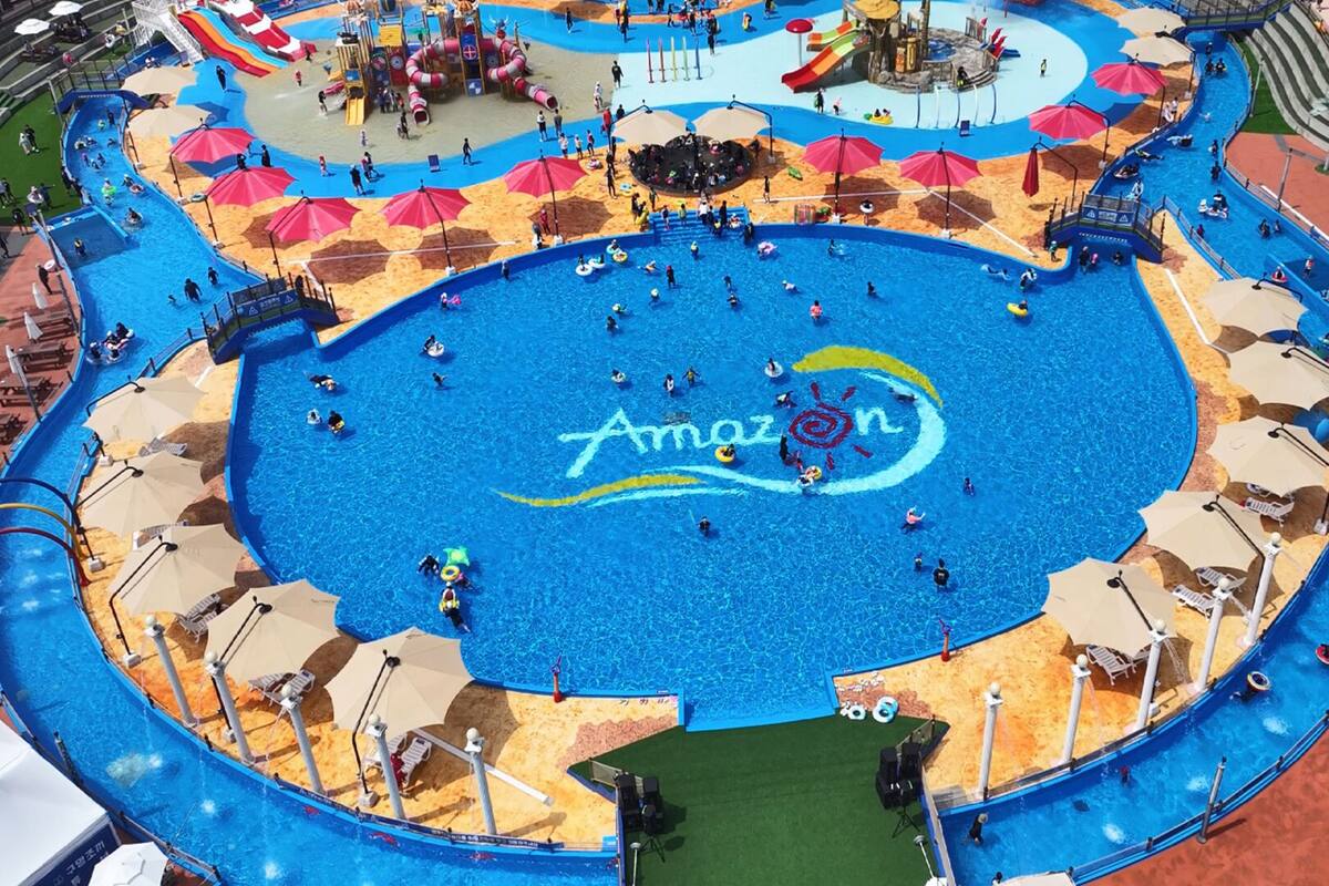 Um parque aquático amplo e coberto, com piscina central e diversas piscinas e áreas de recreação.
