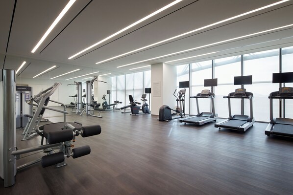 Un gimnasio moderno con varios equipos de ejercicio, amplias ventanas y un diseño limpio y espacioso.