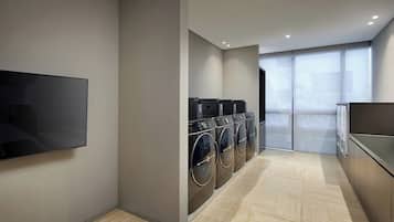 A modern laundry room with a flat-screen TV, multiple washing machines, and a large sliding door leading to a balcony.