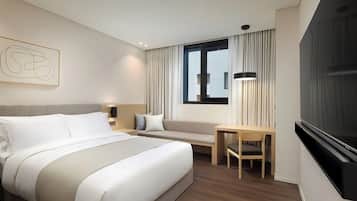Une chambre d’hôtel avec un lit, un bureau, une chaise, une télévision et une fenêtre avec des rideaux.