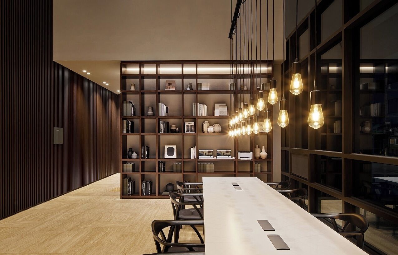 Una sala de conferencias moderna con una larga mesa, sillas y una estantería llena de libros y objetos decorativos.