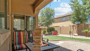 A patio with a fire pit, a striped cushioned chair, and a view of a backyard with a lawn and trees. - Gilbert's Hidden Gem/Pickleball (Gilbert)