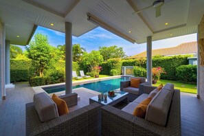 Un espacio exterior cubierto con piscina, mobiliario y abundante vegetación.