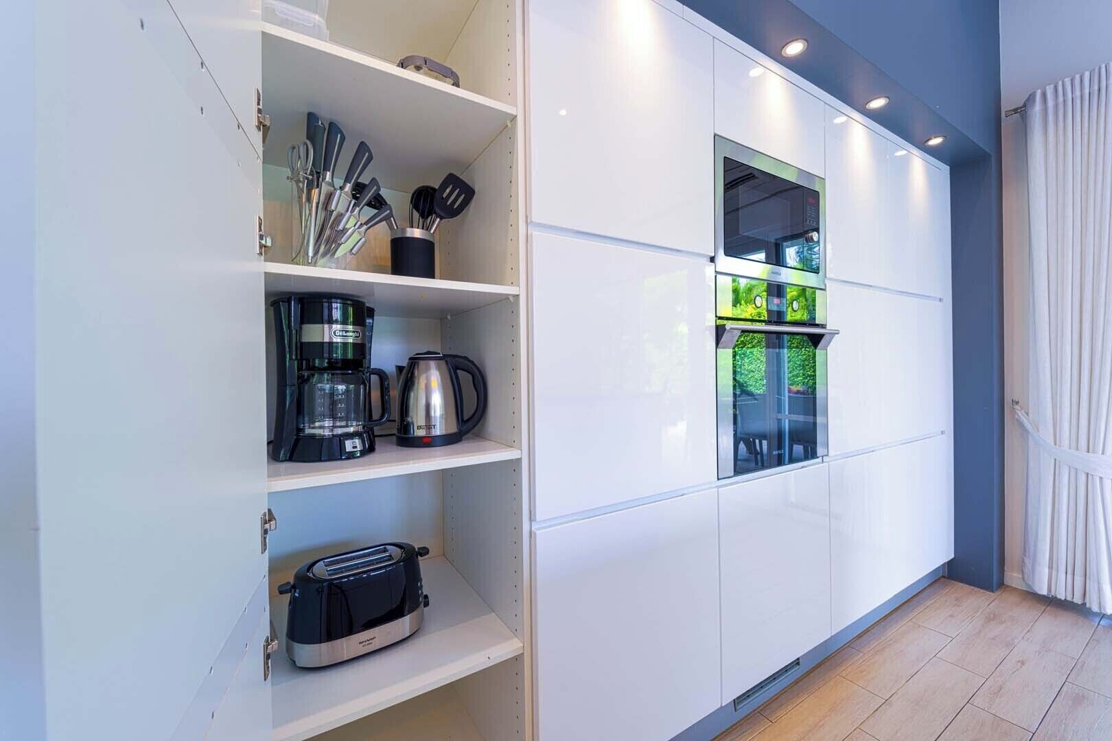 Een moderne keuken met inbouwapparatuur, waaronder een koffiezetapparaat, waterkoker en broodrooster.
