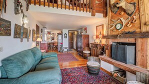 A cozy living room with a green sofa, a patterned rug, wooden accents, a fireplace, and a staircase leading to an upper level. - Grangia Sunset Balcony View for 7 (Sauze di Cesana)
