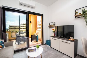 A modern living room with a sofa, a coffee table, a TV, and a sliding glass door leading to an outdoor area. - Always Traveling Near The City Center (Olbia)