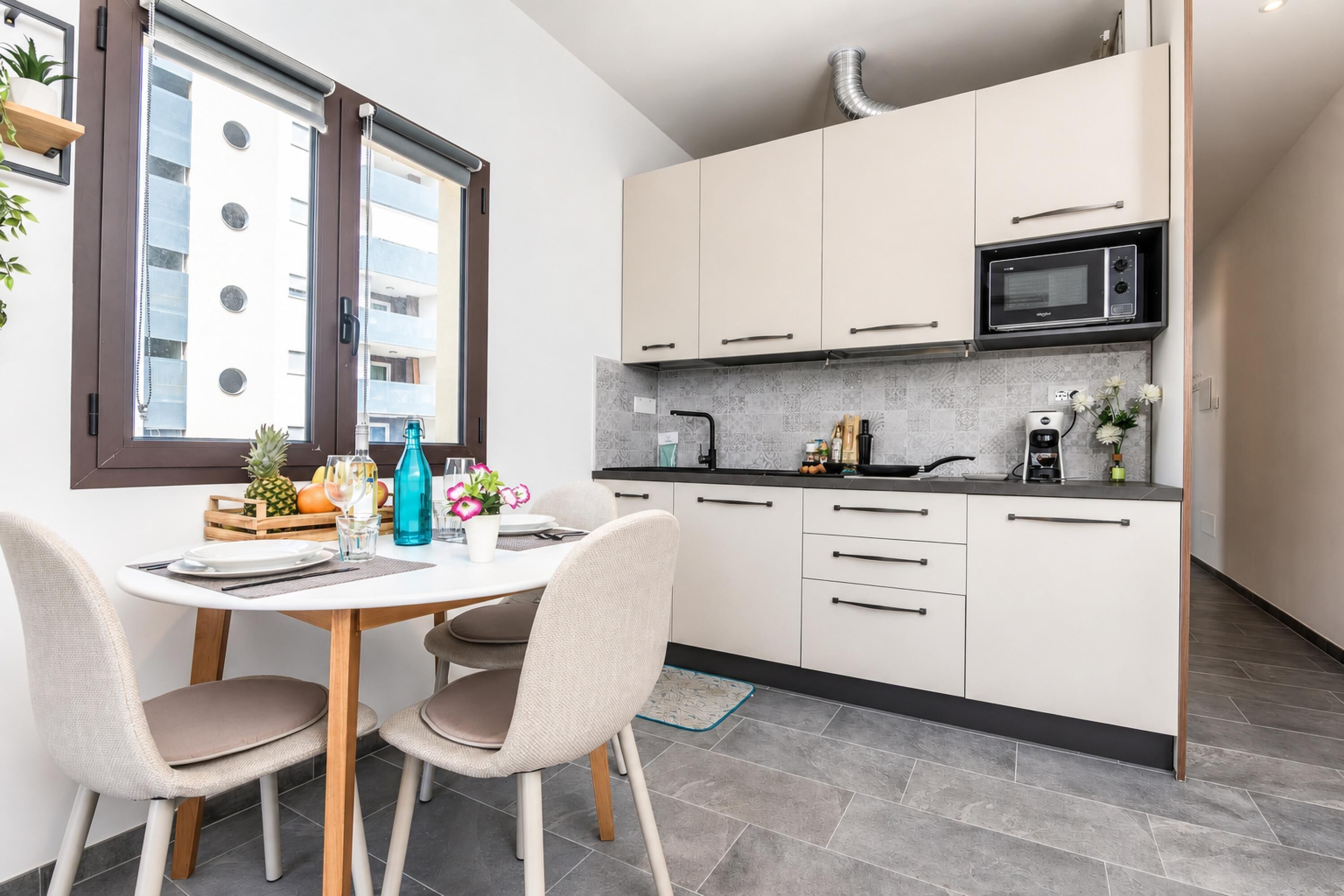 A modern kitchen with white cabinets, a microwave, and a dining area with a table and chairs.