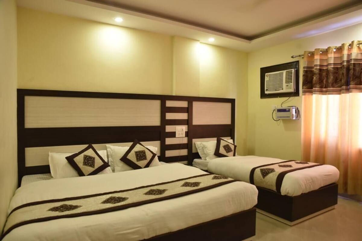 A hotel room with two beds, a large headboard, and a wall-mounted air conditioning unit.