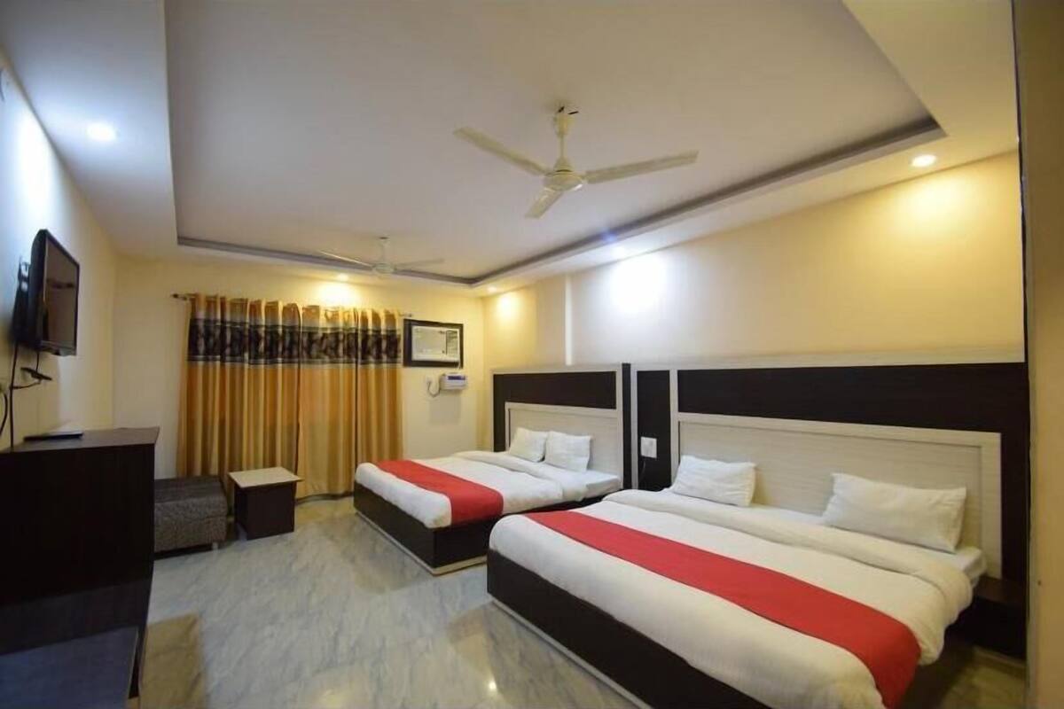 A hotel room with two beds, a desk, a TV, and a ceiling fan.