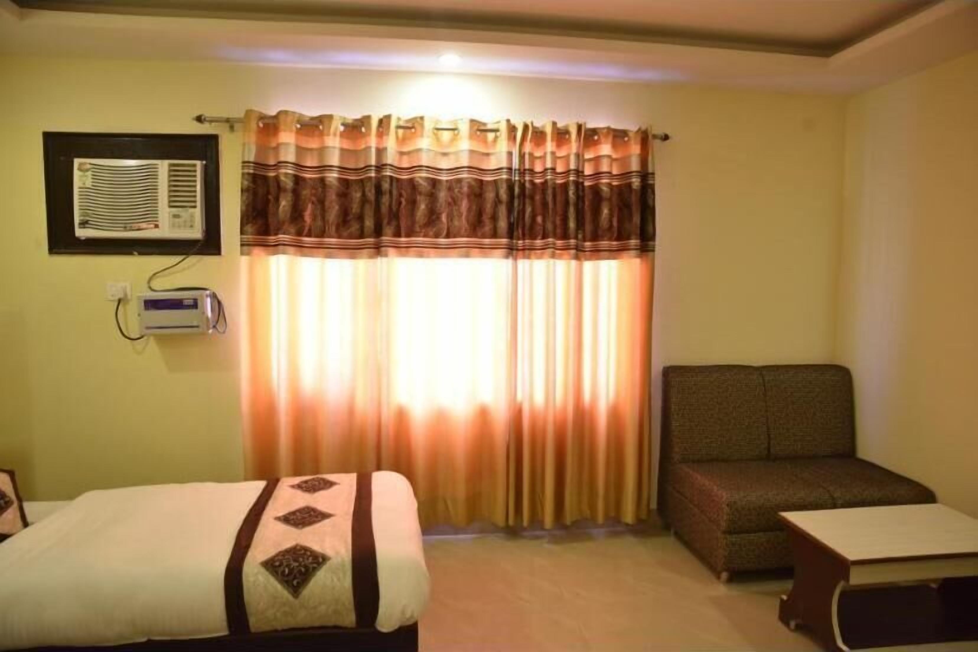 Habitación de hotel con cama, sofá, una mesita, unidad de aire acondicionado y ventana con cortinas.