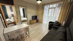 A modern hotel room with a dining area, a sofa, a TV, and a large window with curtains. - Horizon Batumi Aparthotel (Batumi)