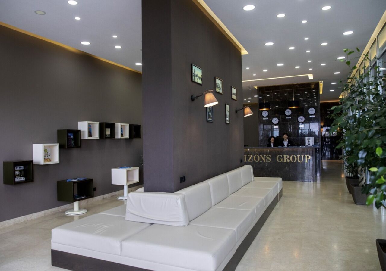 A modern lobby with a reception desk, white sofas, and framed pictures on the walls.