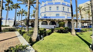 Un hotel de varios pisos con fachada azul y blanca, rodeado de palmeras y un césped cuidado.