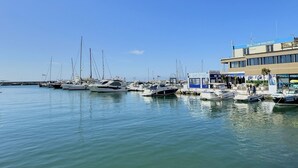 Un puerto deportivo con varios barcos amarrados, un edificio con la inscripción 'Real Club Nautico' y un cielo azul despejado.