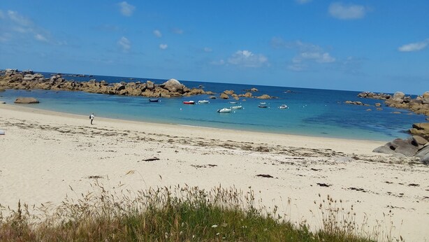 Una playa con agua azul cristalina, afloramientos rocosos y varios barcos.