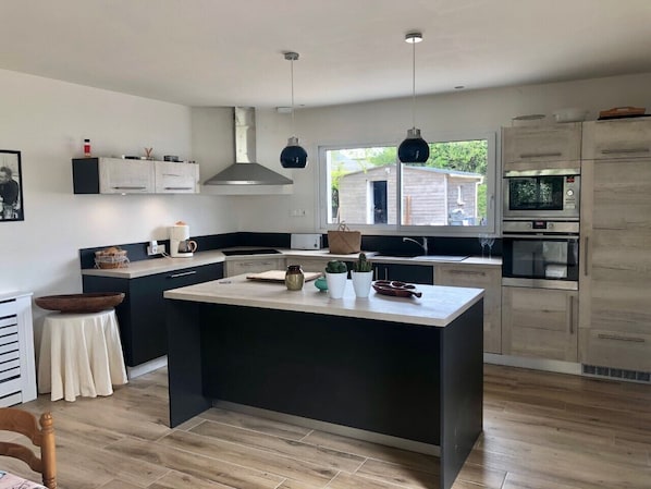 A modern kitchen with a central island, built-in appliances, and a view to the outside.
