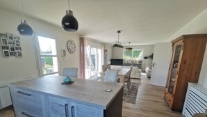 Una cocina amplia con una isla central, un comedor con mesa y sillas, y una sala de estar con sofá y televisor.