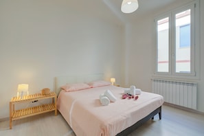 Un dormitorio con cama, mesitas de noche, un radiador y una ventana.