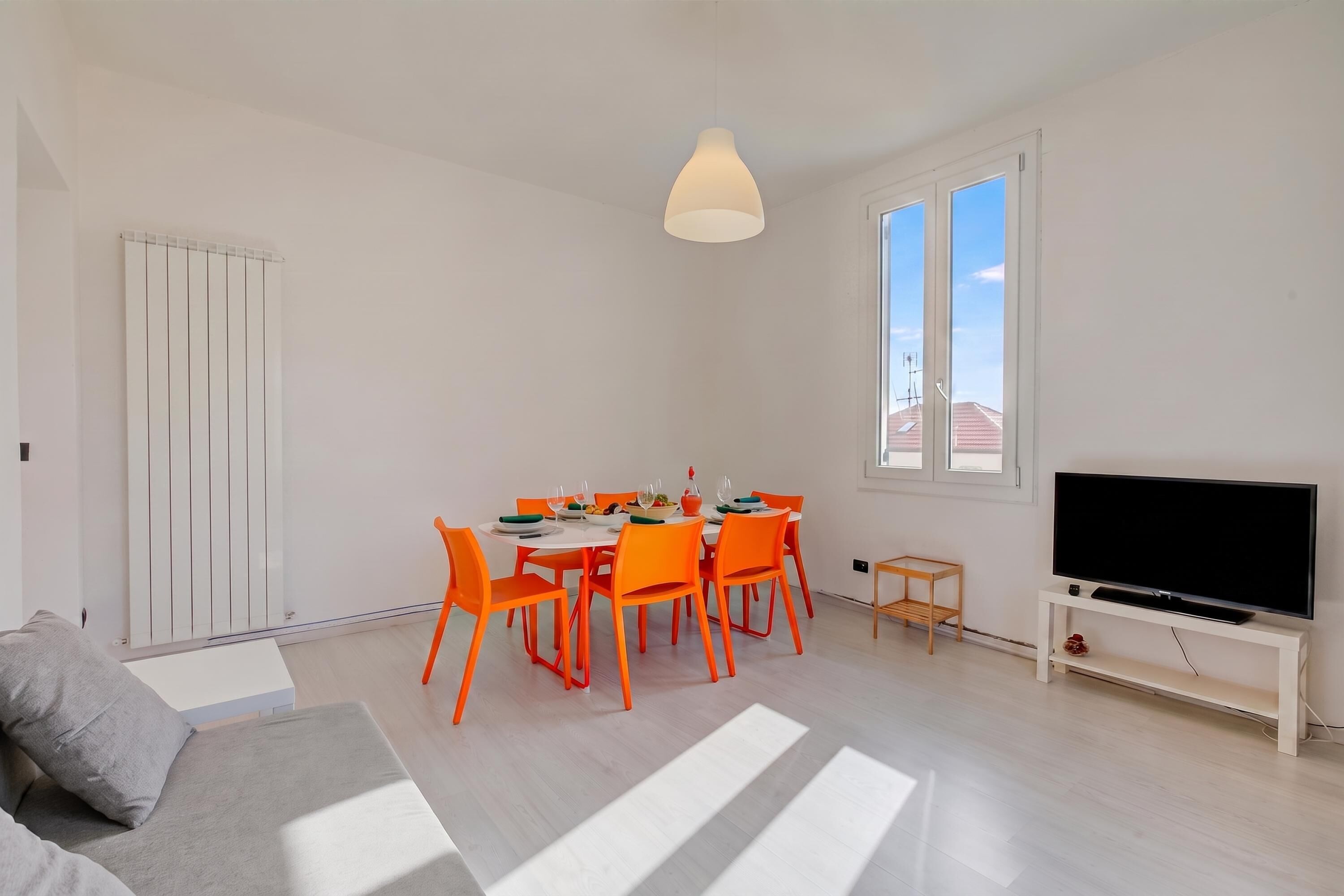 Una sala de estar moderna con comedor, un televisor sobre un mueble bajo y un amplio ventanal.