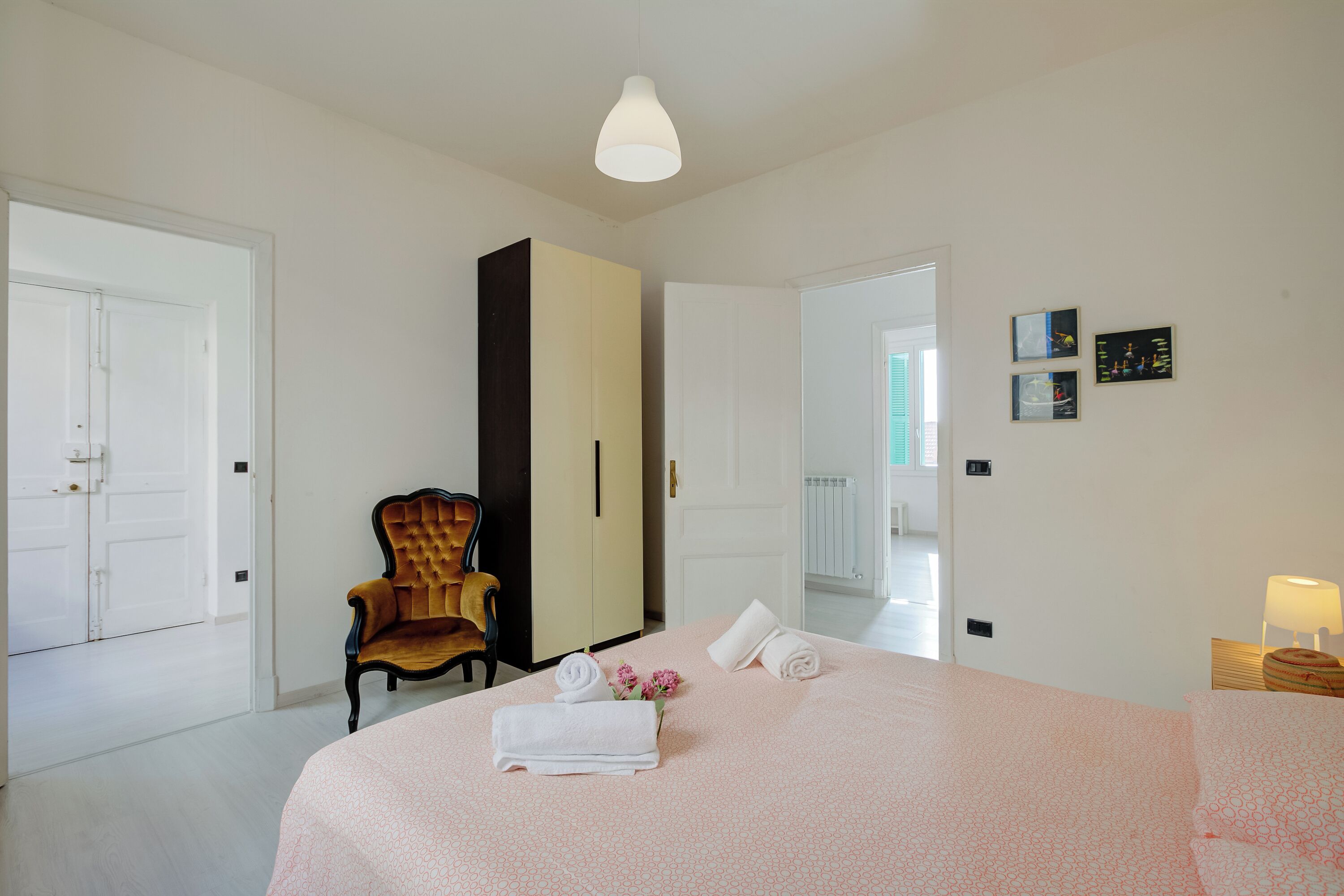 A hotel room with a bed, a chair, a wardrobe, and a nightstand with a lamp.