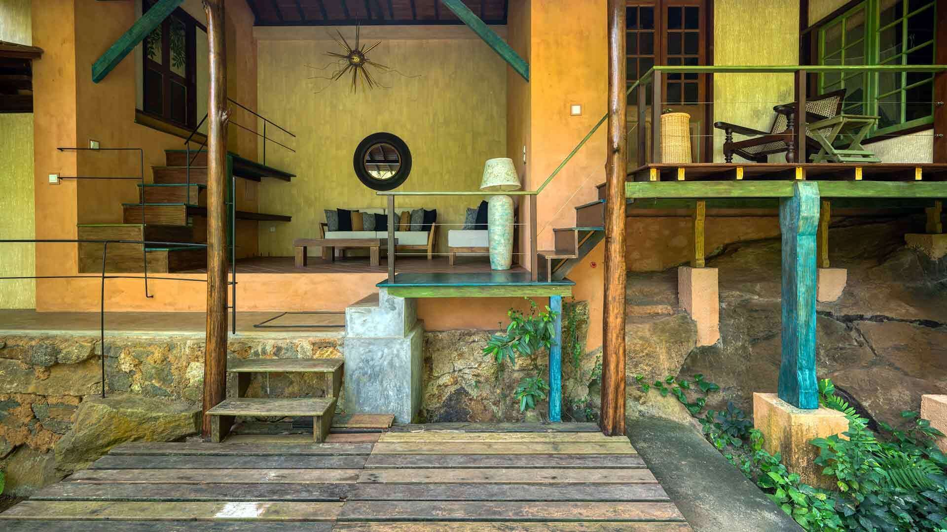 Een rustieke trap die leidt naar een houten terras met uitzicht op een traditioneel ingericht huis.