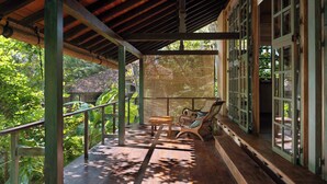 A wooden deck with a bench and table, surrounded by glass doors and windows, overlooking lush greenery. - Sama Retreats - Kosgoda (Kosgoda)