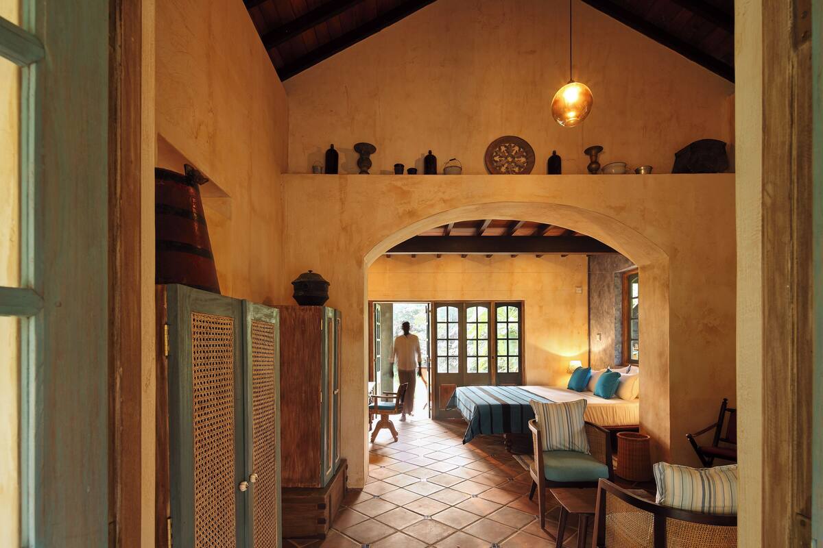 Une pièce spacieuse avec un plafond haut, un lit recouvert d’une courtepointe bleue, une table à manger avec des chaises et un luminaire suspendu.
