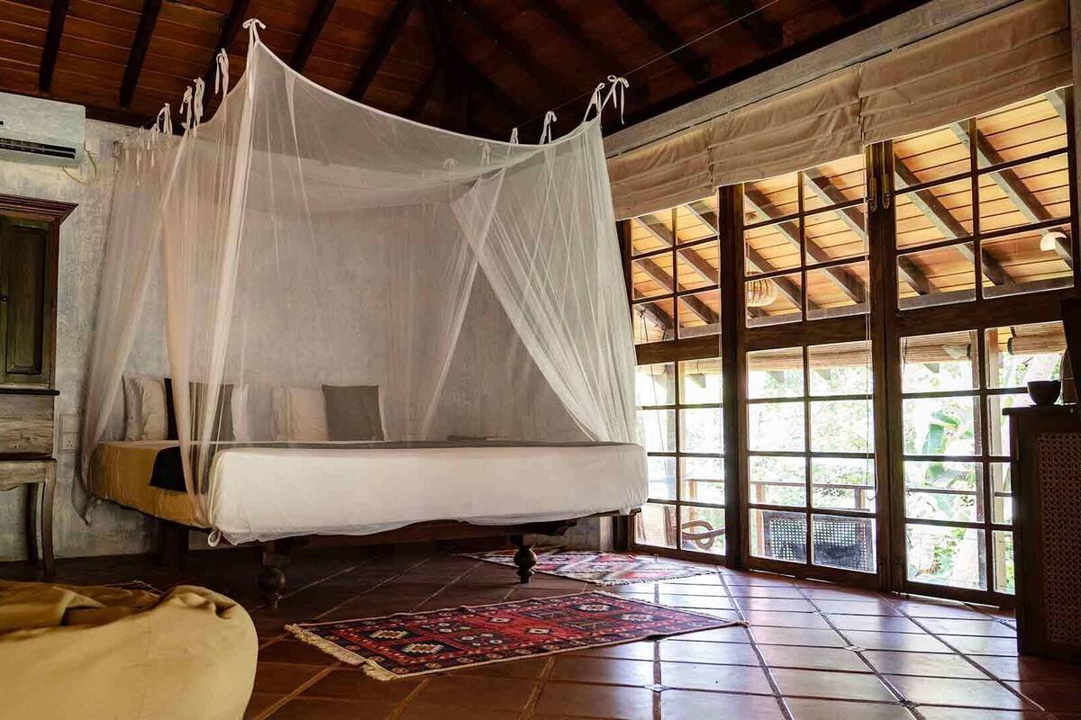 Une chambre avec un lit sous un dais, une armoire en bois et de grandes fenêtres.