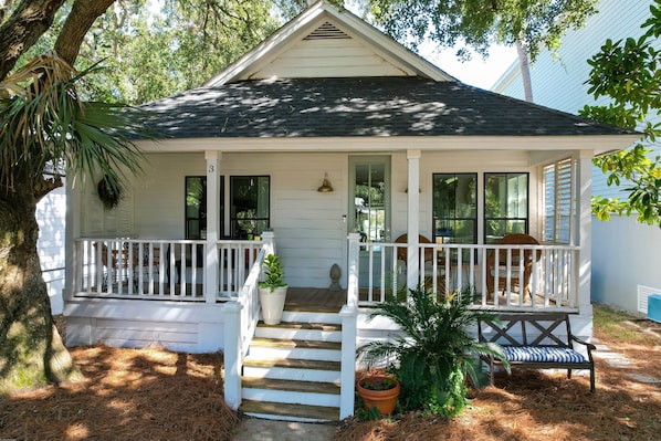 A white house with a porch, steps, and a bench.