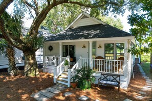 A small white house with a porch, steps, and a bench.