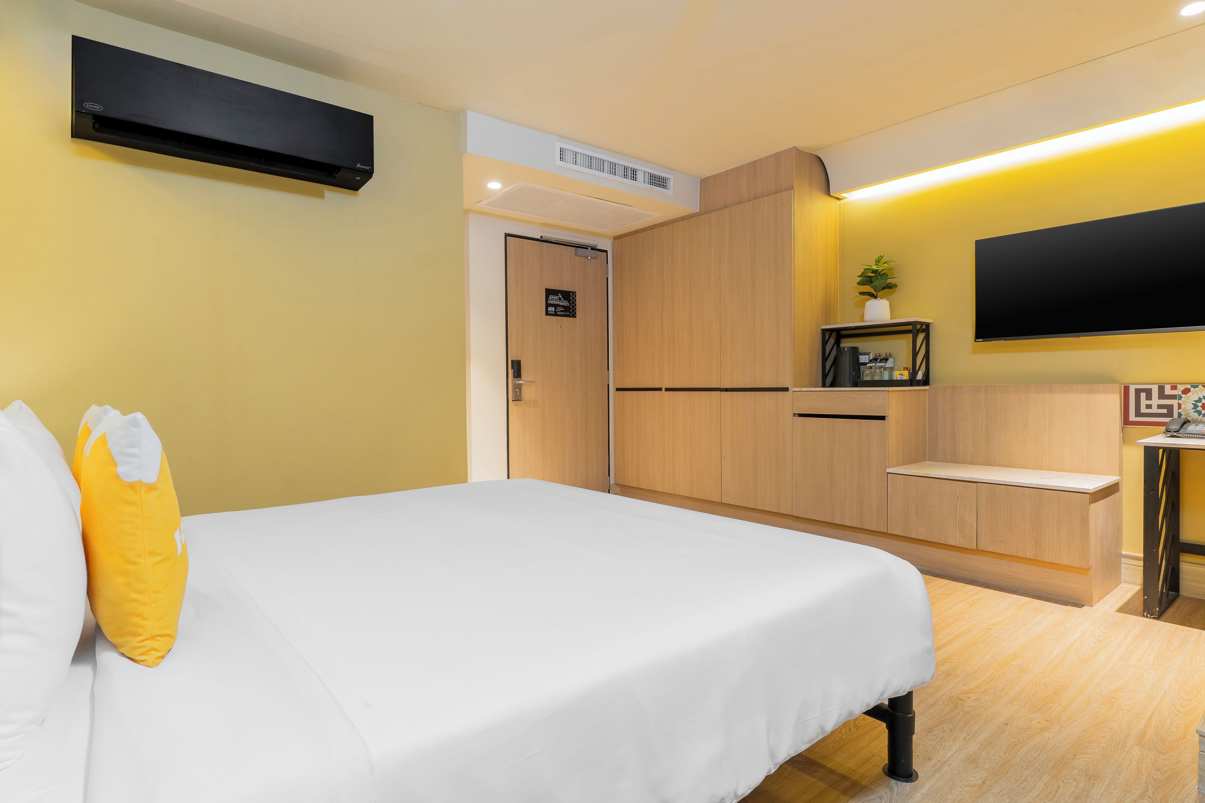 A hotel room with a bed, a flat-screen TV, a wooden wardrobe, and a small table with a plant.