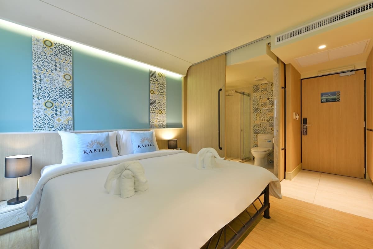 Une chambre d’hôtel avec un grand lit, une table de chevet avec une lampe, un espace douche et des toilettes.