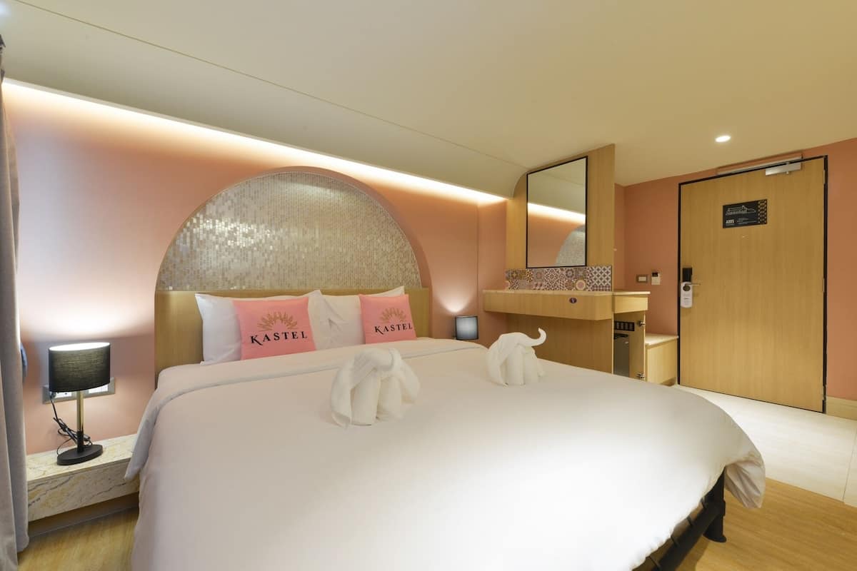 Une chambre d’hôtel avec un grand lit, une tête de lit ornée de motifs en mosaïque, une porte en bois et une petite table de chevet avec une lampe.