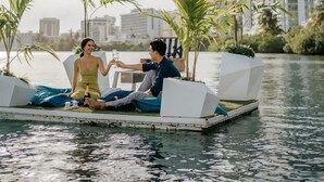 A couple on a floating platform with palm trees and a cityscape in the background. - Beautiful Retreat w. Pool and Perfect Location (San Juan)