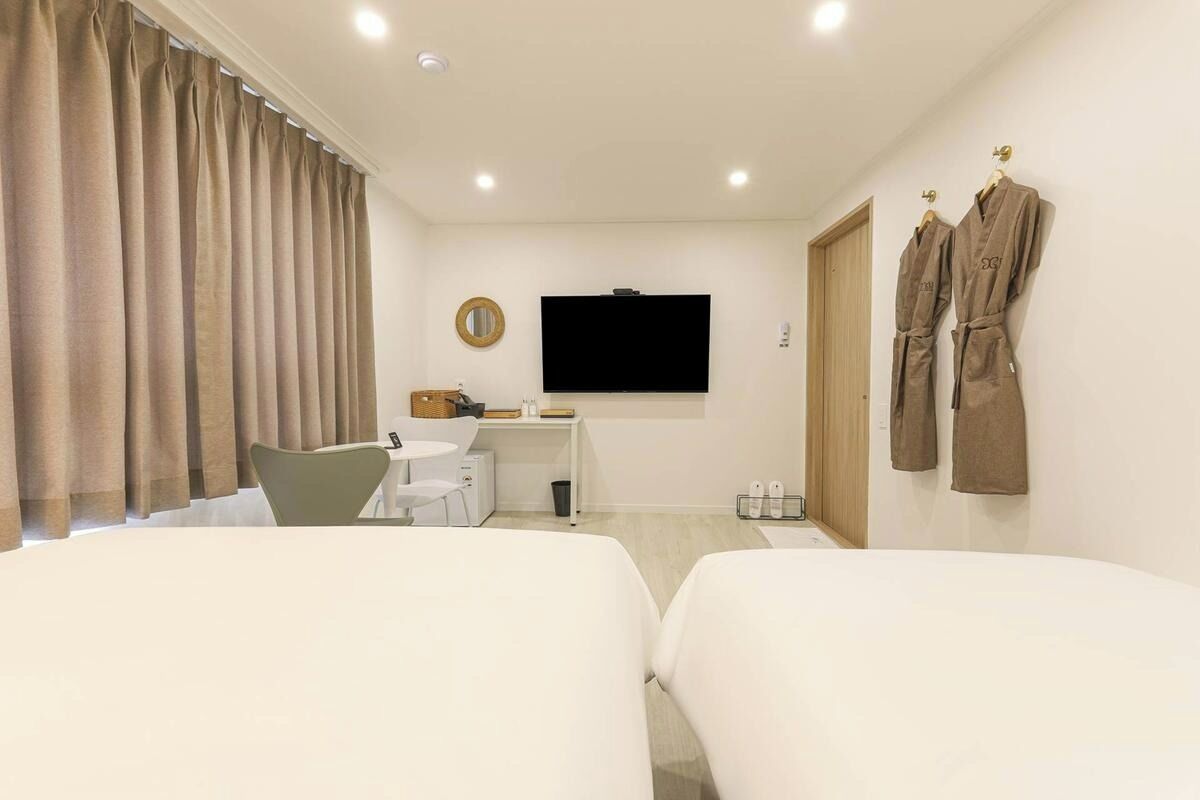 A hotel room with two beds, a desk with a chair, a television, and two robes hanging on the wall.