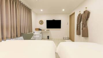 A hotel room with two beds, a desk with a chair, a television, and two robes hanging on the wall.