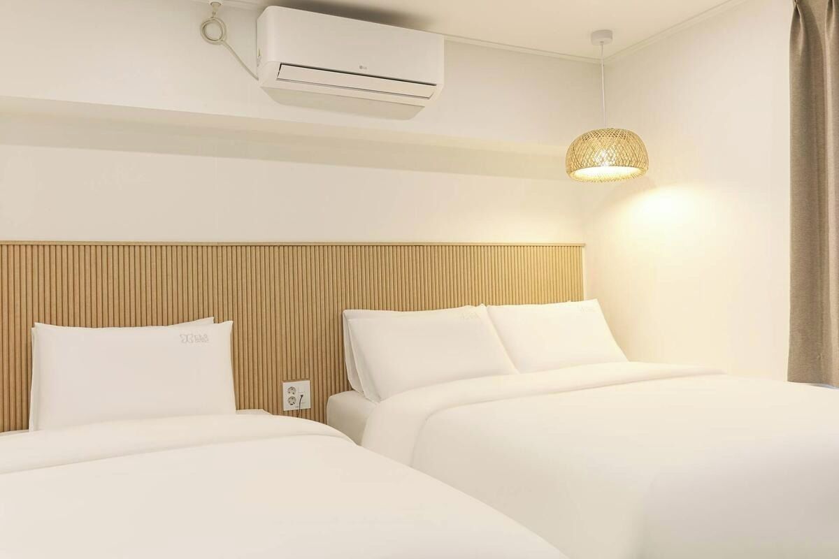 A hotel room with two beds, a wooden headboard, an air conditioner, and a hanging lamp.
