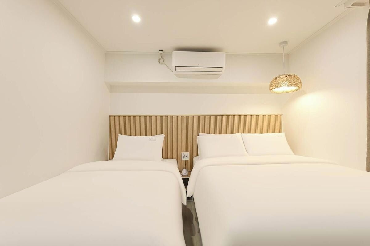 A hotel room with two beds, a wooden headboard, an air conditioning unit, and a hanging light fixture.