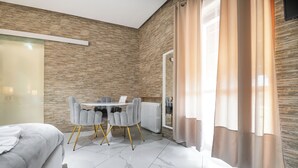 A modern hotel room with a bed, a dining table with chairs, a radiator, and a large window with curtains. - Villa Vitti's - Verona est  (San Martino Buon Albergo)