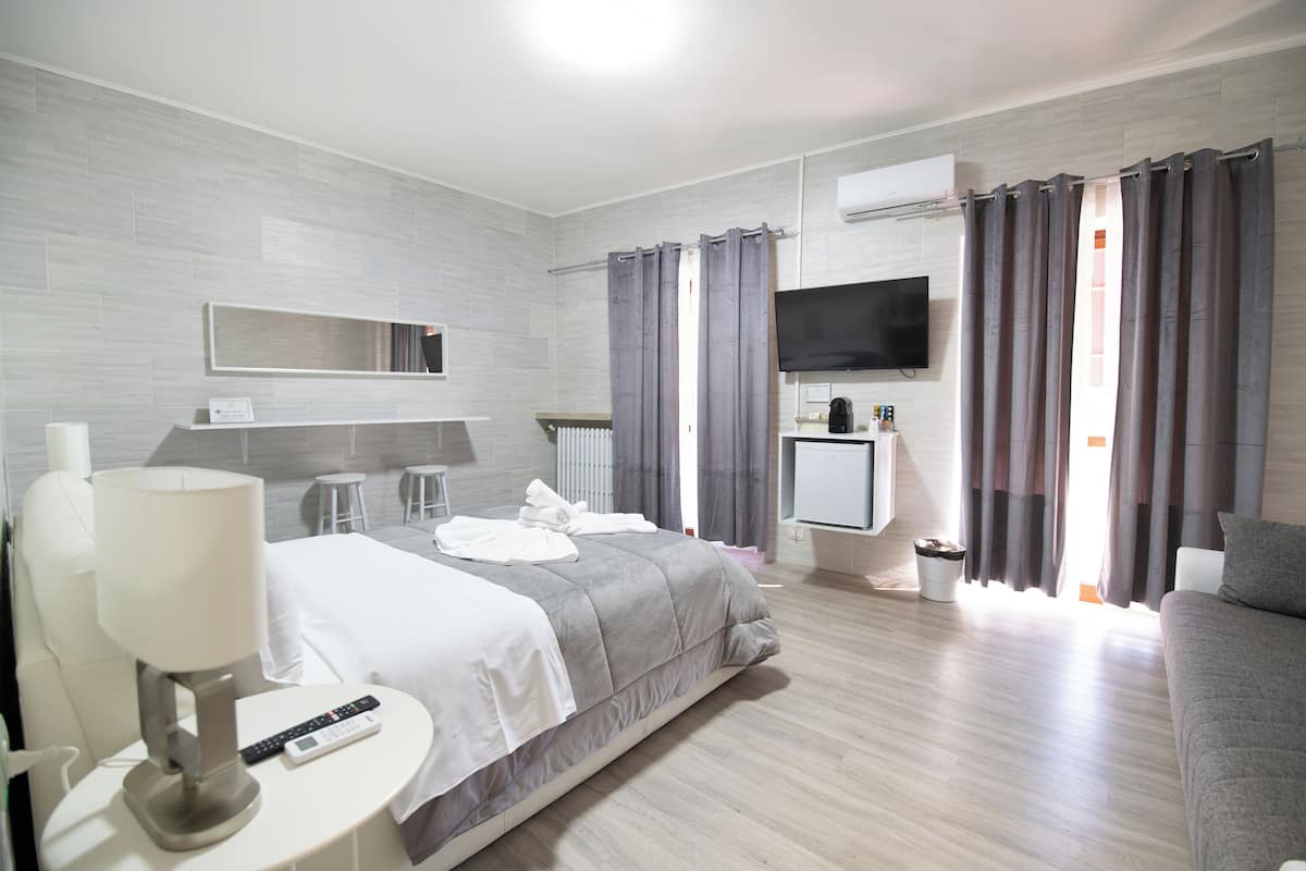 Moderni hotellihuone, jossa on sänky, yöpöytä, lamppu, televisio ja sohva.