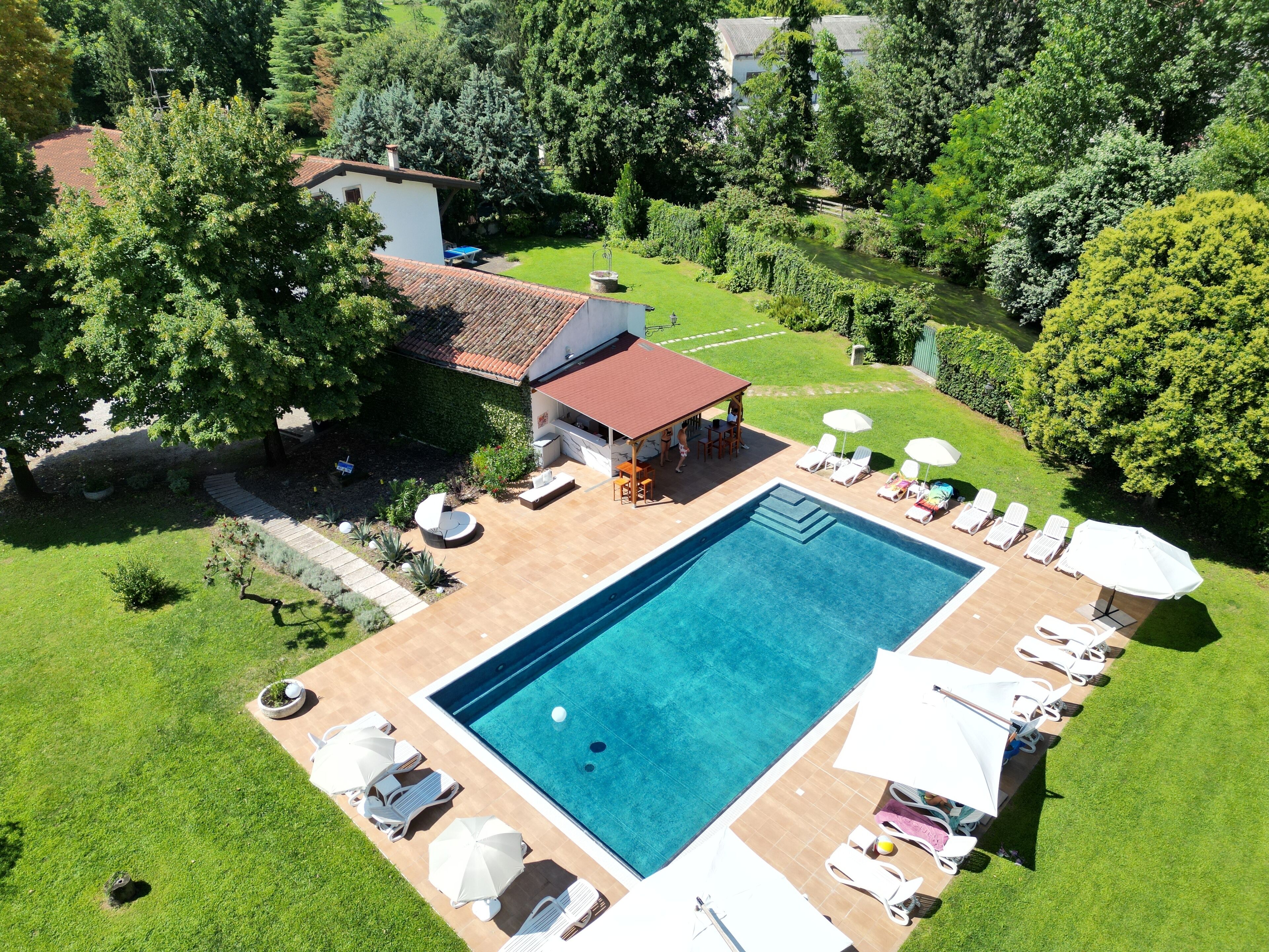 Vue aérienne d’une cour arrière avec une piscine, des chaises longues et un espace barbecue.
