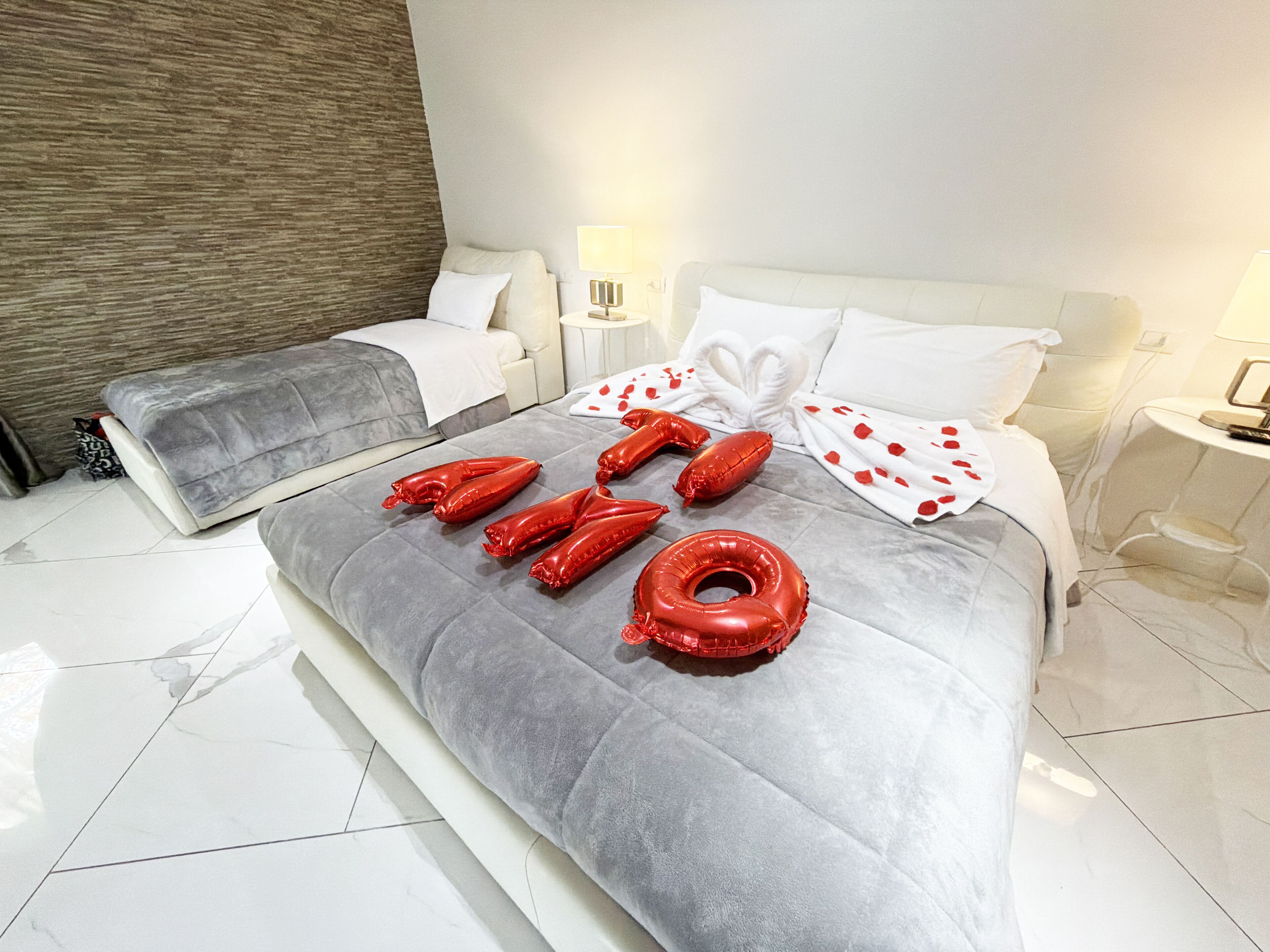 Ein modernes Hotelzimmer mit einem grauen Bett, weißen Kissen und einem Nachttisch mit einer Lampe.