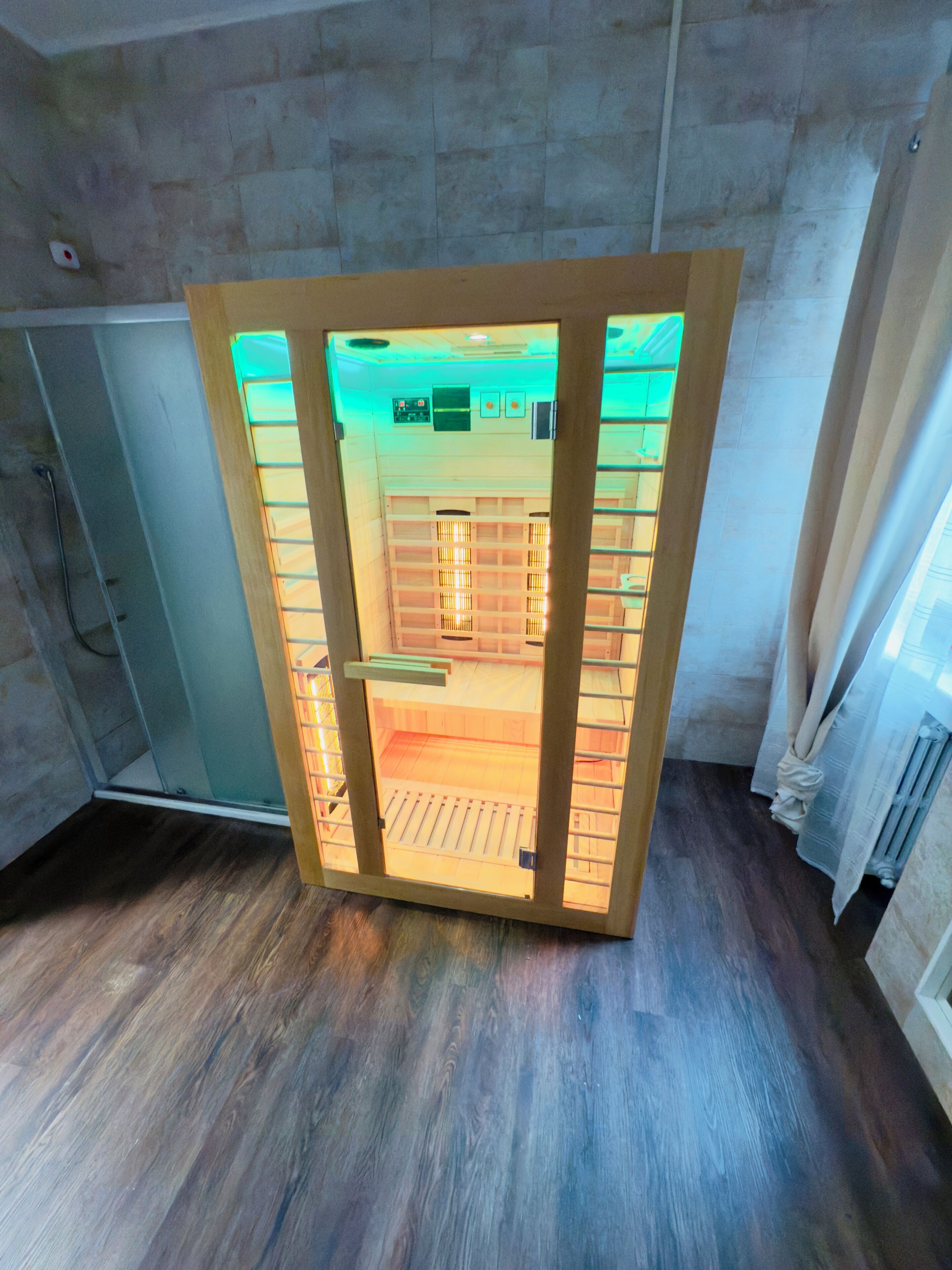 A room with a wooden floor, a glass door with a wooden frame, and a view of a hallway with a tiled wall and a radiator.